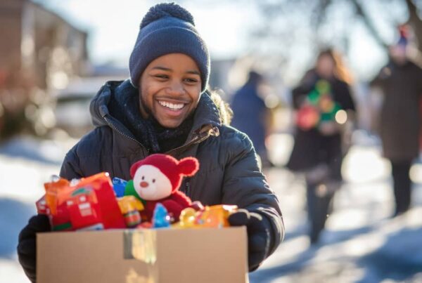 A young man smiling, walking through the snow with a box of gifts.