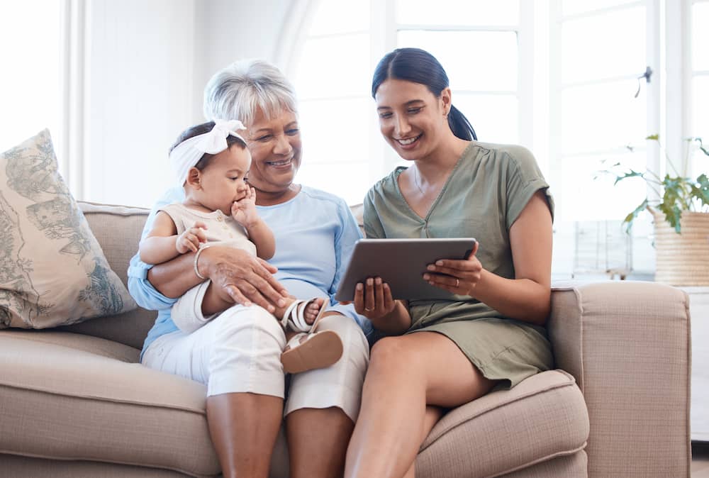 A mother is showing a tablet to grandmother and baby