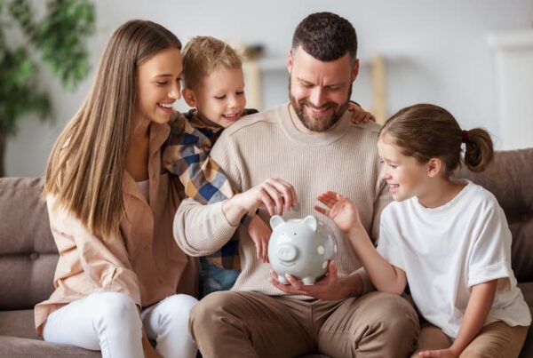 A mother, father, and 2 young children are smiling and gathered around a piggy bank